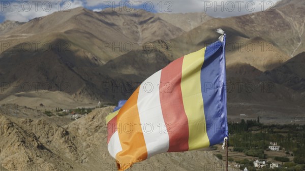 Colorful international Buddhist flag in a mountainous landscape over a green valley, Leh, trekking in Ladakh, Himalayas, India