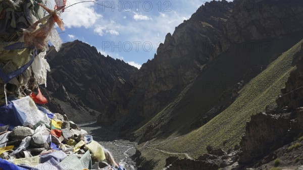 View of a valley with prayer flags and barren mountain landscape under blue sky, trekking at Stok La Pass in Ladakh, Himalayas, India
