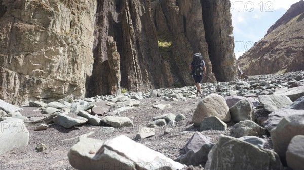 A hiker with a backpack walks through a rocky gorge under a blue sky, trekking at Stok La Pass in Ladakh, Himalayas, India
