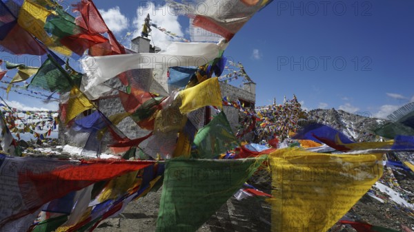 Close-up, colorful prayer flags waving in the wind in front of a temple at Khardung-La Pass in the mountainous landscape under blue sky, trekking in Ladakh, Himalayas, India