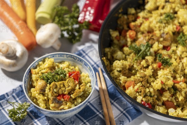 Bowl of fried rice and chopsticks next to pan and fresh ingredients