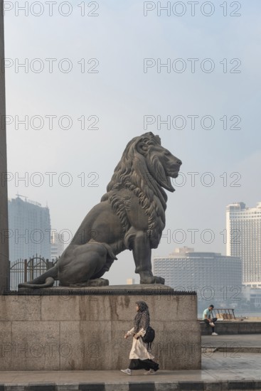 Cairo, Egypt. July 1st 2024 A woman walks past one of the famous bronze lions guarding Qasr El Nil Bridge over the River Nile in Downtown Cairo, Egypt