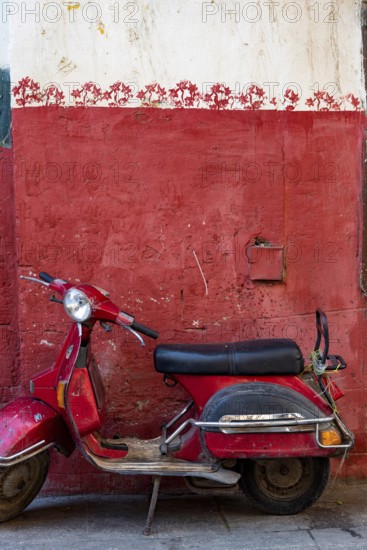 Cairo, Egypt. November 26th 2022 Cute red motor scooter parked against a red painted wall in the Islamic quarter of Cairo near the Khan el Khalili Bazaar, Egypt