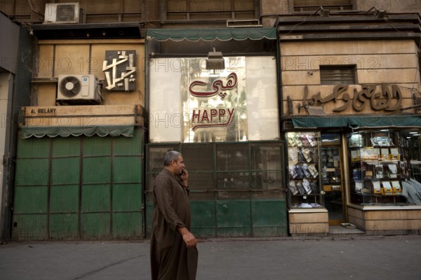 Cairo, Egypt. June 14th 2024 Typical Downtown Cairo street scene as an Egyptian man walks past shops while talking on a mobile phone wearing traditional clothes