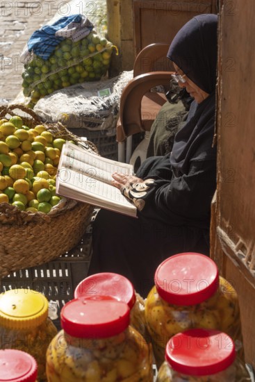 Cairo, Egypt. December 7th 2022 An Egyptian woman reading a book while selling fruit and vegetables on the street in Islamic Quarter of Cairo, Egypt