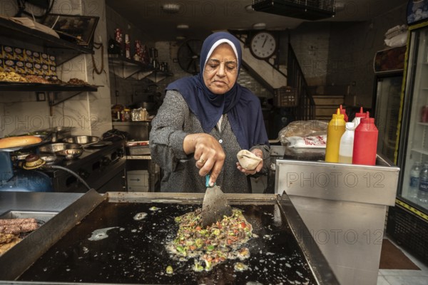 Cairo, Egypt. November 30th 2022 An Egyptian woman frying hot green peppers and chopped liver to make liver sandwiches a popular Egyptian street food snack, Cairo, Egypt