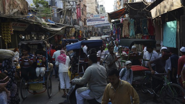 Bustling street scene with bicycle rickshaws and people in a busy market, Delhi, India