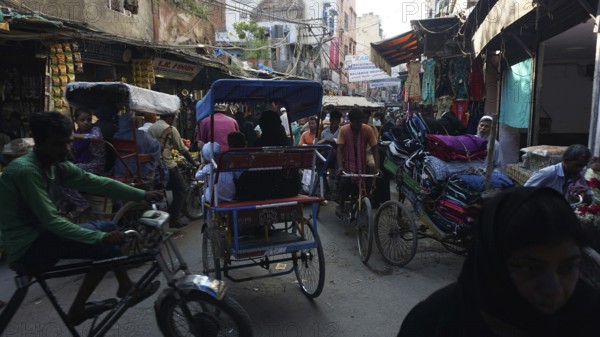 Lively urban street scene with bicycle rickshaws and hustle and bustle at a market, Delhi, India