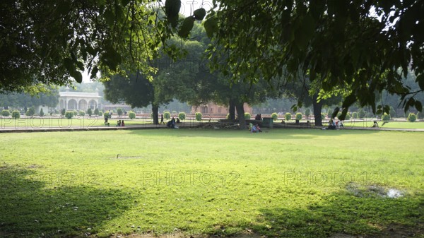 Green garden with trees in shade, people relaxing on the lawn of Red Fort in Delhi