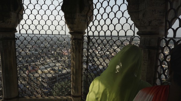 View of Delhi through an ornate grid from the mosque tower with two people in traditional dress, Delhi, India