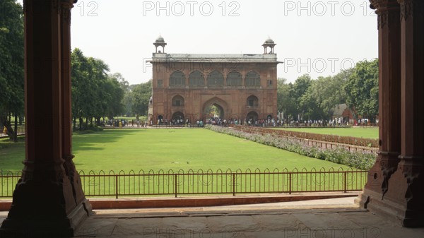 Historic gate with green lawn and trees, Red Fort in Delhi with numerous visitors in the area, Delhi, India