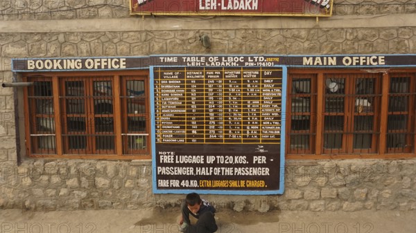 Stone building at the bus terminal with a large timetable on the façade and signs for Leh, Ladakh, North India, Himalayas, India