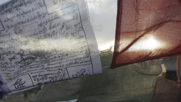 Prayer flags waving in the wind with texts and translucent sun in the background, Leh, Ladakh, North India, Himalayas, India