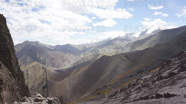 Panoramic view of a mountainous landscape with rolling hills and snow-capped peaks on the horizon, trekking at Stok La Pass in Ladakh, Himalayas, India