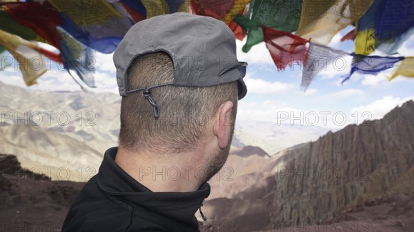 Person looking at a vast mountain landscape under fluttering prayer flags, trekking at Stok La Pass in Ladakh, Himalayas, India