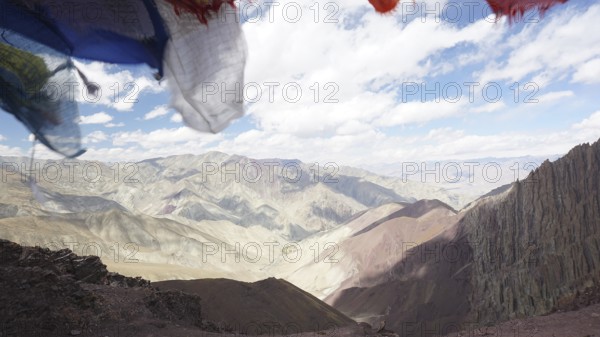Prayer flags in front of a vast, cloud-covered mountain landscape, trekking at Stok La Pass in Ladakh, Himalayas, India