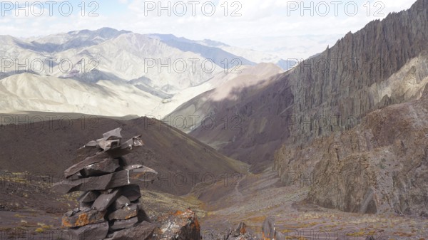 Stone tower as a guide with a view of extensive, rocky mountain landscape, trekking at Stok La Pass in Ladakh, Himalayas, India