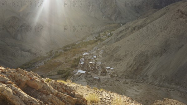 Rays of light illuminate a remote village in a valley between bare mountains, trekking in Ladakh, Himalayas, India