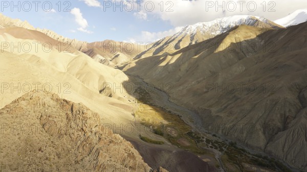 Spectacular panorama of a sunny valley crossed by barren mountains, illuminated by dramatic lighting conditions, trekking at Stok La Pass in Ladakh, Himalayas, India