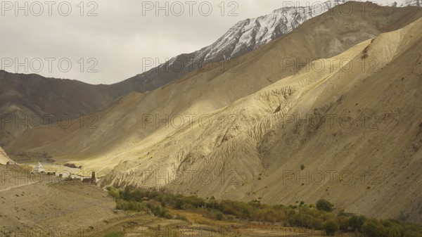 Wide valley with dramatic, barren mountain landscapes under cloudy sky, trekking in Ladakh, Himalayas, India