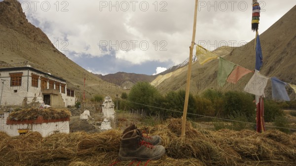 Mountain boot, hiking boots next to prayer flags against mountainous landscape with turbulent clouds, trekking in Ladakh, Himalayas, India