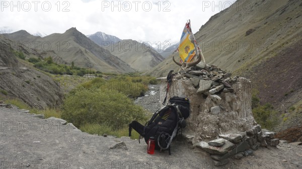 Place of worship with colorful flags and backpack in a mountainous landscape, break on a trekking tour, Ladakh, Himalayas, India