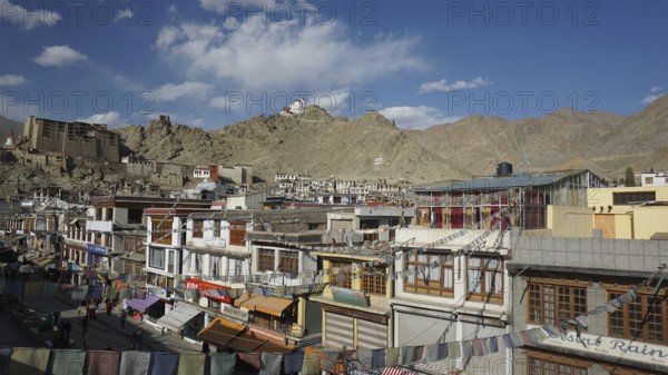 View of Leh pedestrian street with traditional buildings, Leh Palace and mountain scenery in the background, Ladakh, Himalayas, India