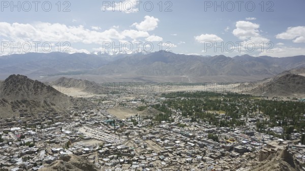 Long-range city view with mountains and sky in the background under white cloudy sky, Ladakh, Himalayas, India