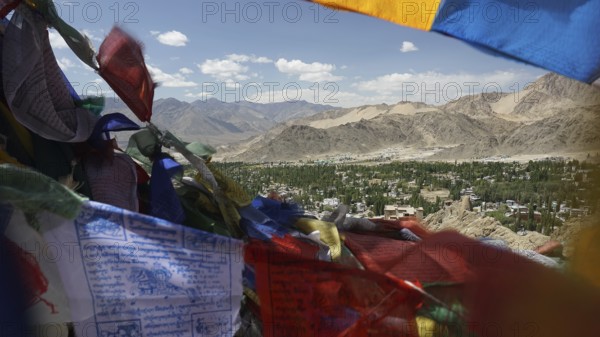 Colourful prayer flags in front of a vast valley and mountain landscape under clear skies, Ladakh, Himalayas, India