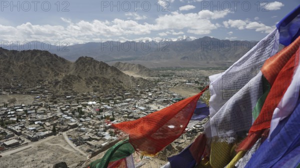 City view with prayer flags in the foreground and mountain scenery in the background under blue sky, Ladakh, Himalayas, India