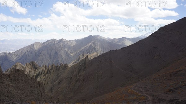 Rocky mountain range under cloudy sky and wide valley, trekking at Stok La Pass in Ladakh, Himalayas, India