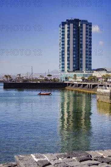 Modern high-rise building reflected in calm water, urban ambiance under clear skies, Arrecife, Lanzarote, Canary Islands, Spain