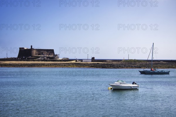Historic Castillo de San Gabriel fortress by the sea, two boats on blue water under clear skies, Arrecife, Lanzarote, Canary Islands, Spain