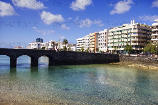 Historic bridge over clear water with modern buildings in the background under blue sky, Arrecife, Lanzarote, Canary Islands, Spain