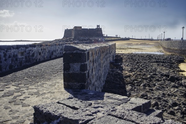 Stone path leads to the historic Castillo de San Gabriel fortress with a view of the sea under a blue sky, Arrecife, Lanzarote, Canary Islands, Spain
