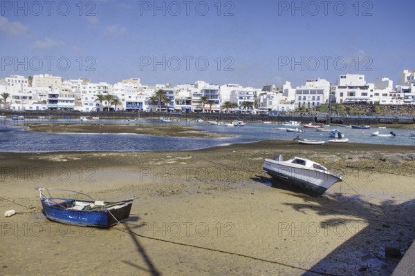 Boats on the banks of Charco de San Ginés lagoon in front of white buildings under blue sky, Arrecife, Lanzarote, Canary Islands, Spain