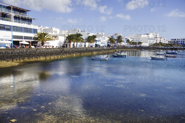 Boats on the calm waters of the Charco de San Ginés lagoon surrounded by palm trees and white buildings, Arrecife, Lanzarote, Canary Islands, Spain