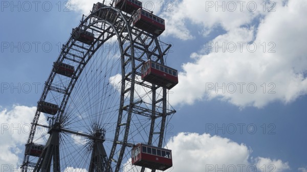 A big Ferris wheel with red cabins under a blue, cloudy sky, Prater, Vienna