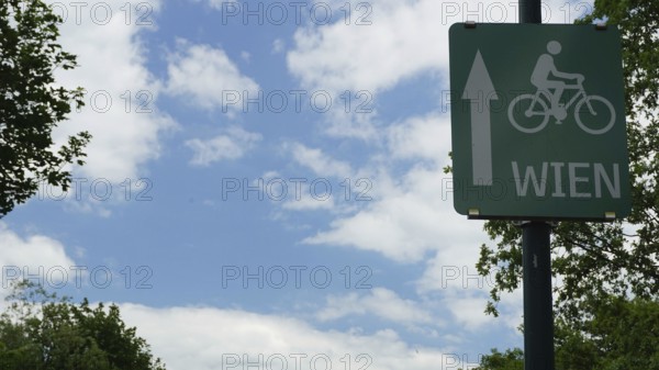 Bicycle trail sign to Vienna in front of a cloudy sky and trees, Danube Cycle Route, Austria