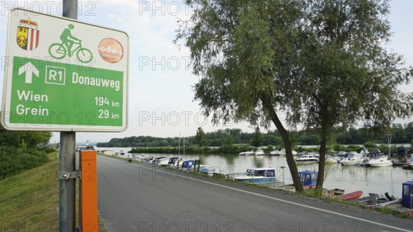 Signpost on Danube trail R1 with river and boats in the background, cycling on the Danube cycle path, Danube, Germany