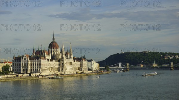 Large parliament building in Budapest on the banks of the Danube under blue sky with bridge in the background, Budapest, Hungary