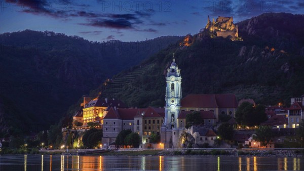 Illuminated church and castle in Dürnstein in front of a hill at dusk, reflected in the river, Danube cycle path, Wachau World Heritage Region, Austria
