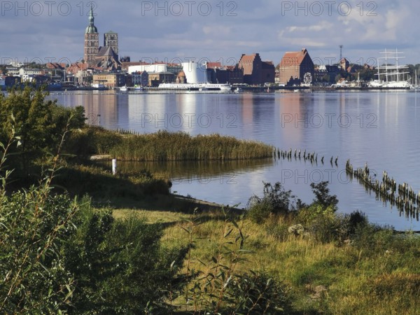 City view of Stralsund, with lakeside churches, green meadows and ships on a cloudy day