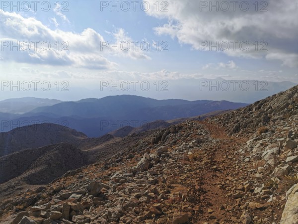 Rocky mountain trail with views of surrounding mountains and clouds, climbing Tahtali Dagi, Lycia, Turkey