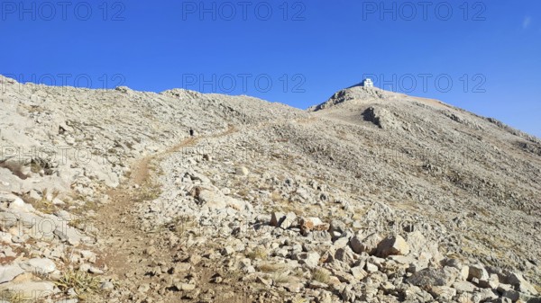 A trail snakes over a rocky mountainside up to the summit of Tahtali with clear skies, climbing Tahtali Dagi, Lycia, Turkey