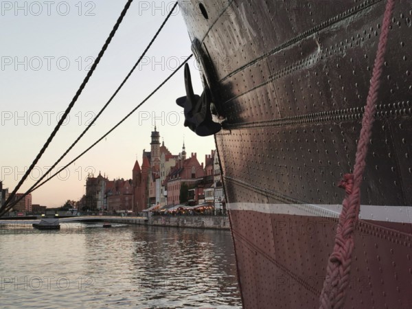 Looking along the bow, a large ship is moored in the harbor in front of the picturesque, historic city of Danzig in the evening light, Baltic Sea, Danzig, Poland