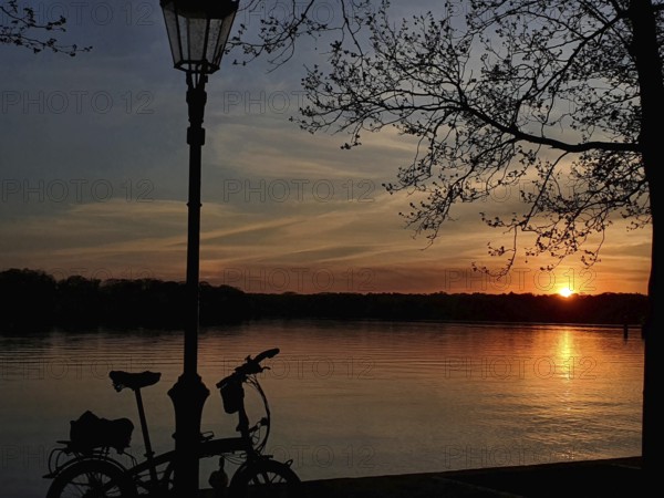 Sunset on the waterfront with silhouette of a bicycle leaning against a lantern, Tegeler See, Berlin