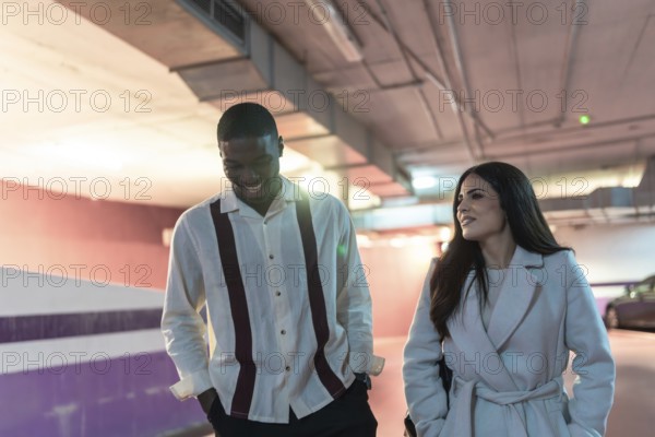 Diverse couple happily walking through an underground car park, enjoying their date while having a conversation and smiling, creating a sense of togetherness and urban lifestyle