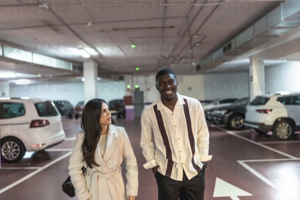 Young interracial couple walking and smiling together in an underground parking garage, looking around for their car or an exit after shopping or an event