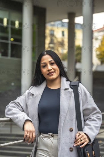 Confident indian woman showing her elegant business casual style, leaning on a railing in an urban street, representing professionalism and success outdoors